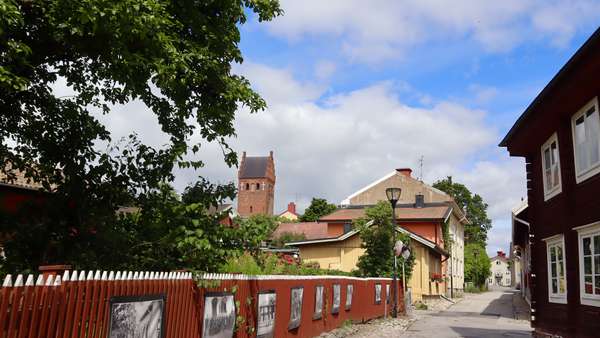  A red fence to the left in the image, older wooden houses, and a red church in the background.